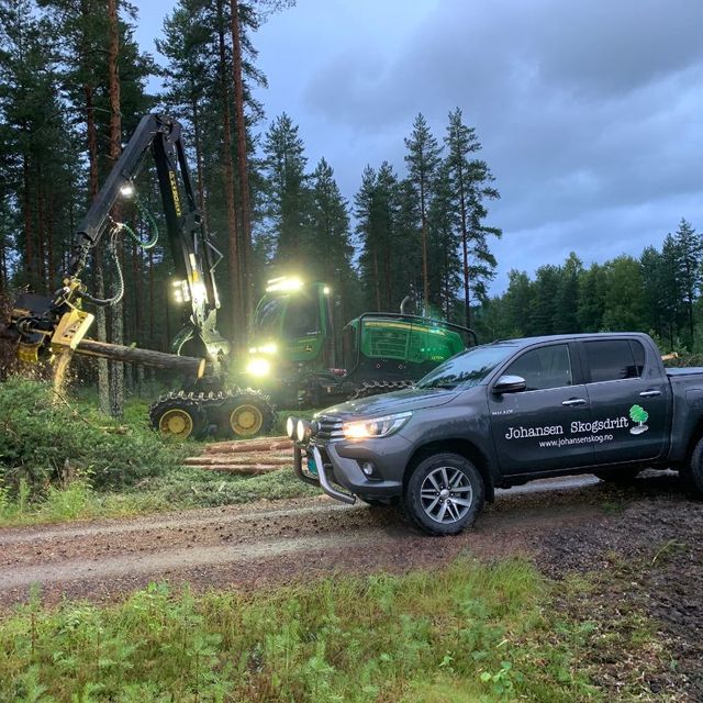 Arbeidsbil og stor maskin i skog på kveldstid